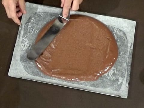 La pâte à biscuit chocolat est étalée sur la plaque à pâtisserie graissée recouverte d'une feuille de papier sulfurisé, à l'aide d'une spatule métallique coudée