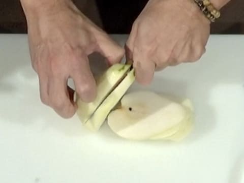 Une poire est taillée en tranches à l'aide d'un couteau, sur une planche à découper