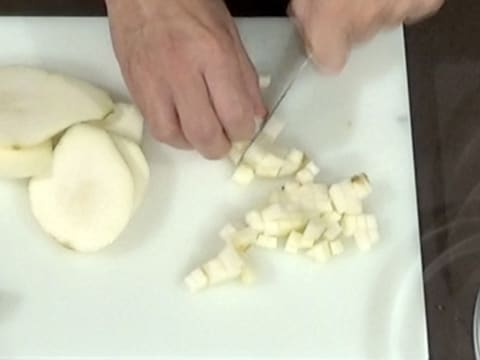 Les bâtonnets de poire sont taillés en petits cubes à côté des tranches de poire sur la planche à découper