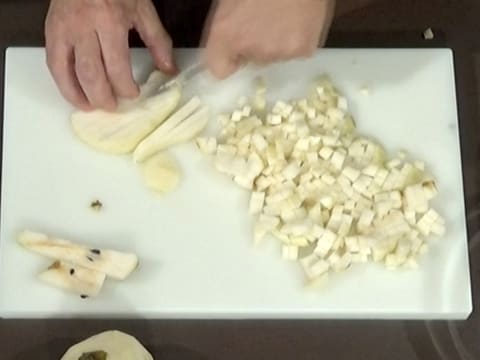 La dernière tranche de poire est taillée en bâtonnets à côté des petits cubes de poire sur la planche à découper