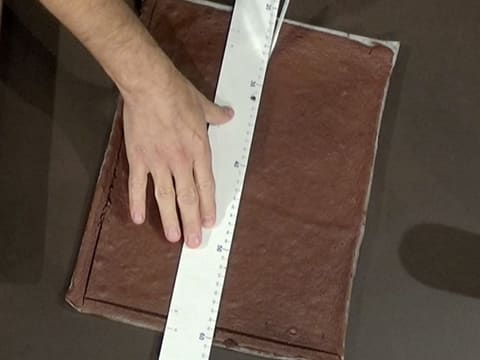 Le biscuit qui se trouve sur la plaque à pâtisserie, sur le plan de travail, est découpé à l'aide d'un couteau et d'une règle graduée