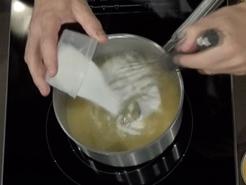 Le sucre en poudre est versé sur la purée de poire dans la casserole, tout en étant mélangé au fouet