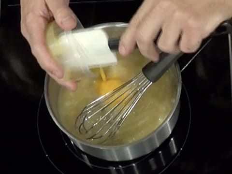 Ajout des jaunes d'oeufs dans la casserole contenant la purée de poire et le sucre en poudre, ainsi que le fouet posé dedans