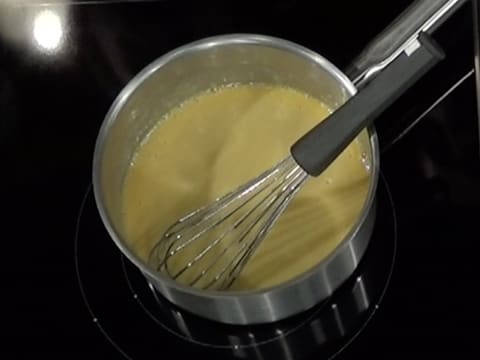 La casserole contenant la préparation à la poire et le fouet est sur la plaque de cuisson