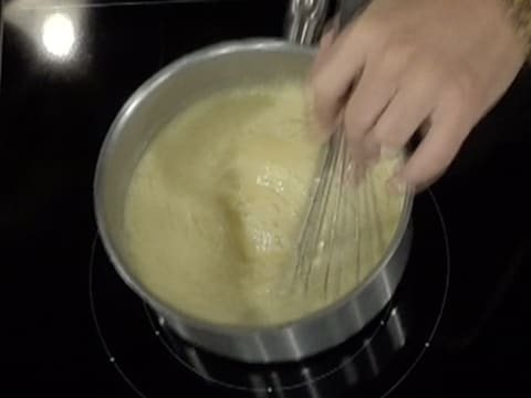 La préparation à la poire est en train de cuire et d'être mélangée au fouet, dans la casserole sur la plaque de cuisson