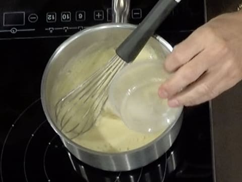 La gélatine en poudre hydratée est versée dans la crème à la poire qui se trouve dans la casserole, sur la plaque de cuisson