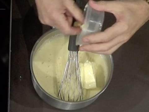 Ajout du beurre pommade dans la casserole qui contient la crème à la poire et le fouet posé dedans