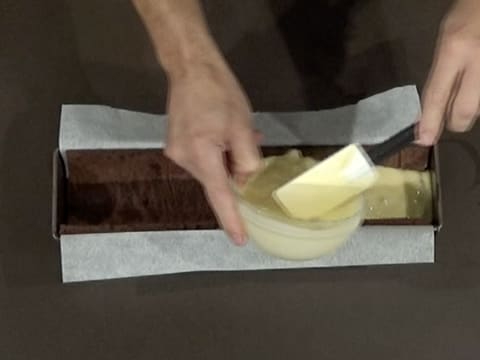 Le mélange crémeux poire et cubes de poire est versé sur la bande de biscuit chocolat qui est moulé dans le moule à bûche chemisé d'une feuille de papier sulfurisé