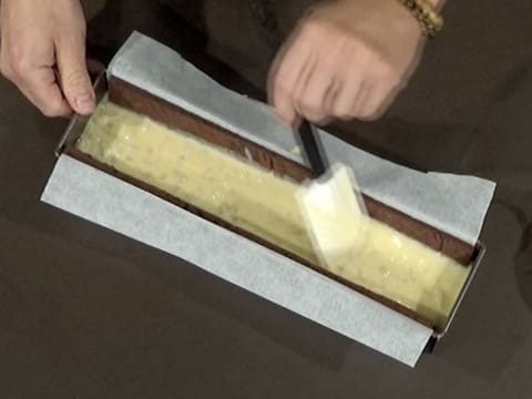 La surface du crémeux poire est lissée avec la spatule maryse, dans le moule à bûche chemisé contenant le biscuit chocolat