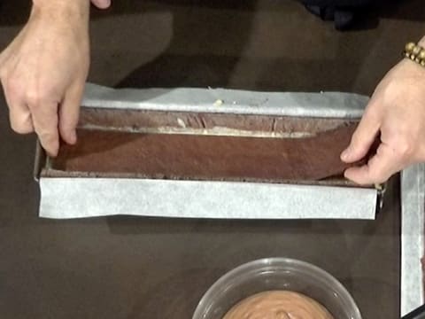 Une bande de biscuit chocolat est placé dans le moule à bûche chemisé, sur le crémeux poire