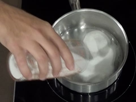 Ajout du sucre en poudre dans l'eau contenue dans la casserole qui est placée sur la plaque de cuisson