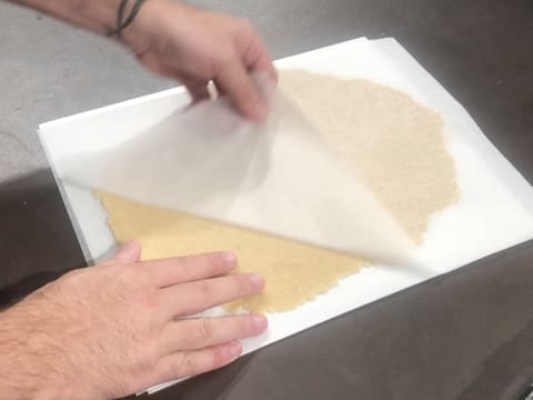 La pâte à streusel amande est abaissée de façon verticale au rouleau à pâtisserie, entre deux feuilles de papier sulfurisé et entre deux réglettes à niveler violettes