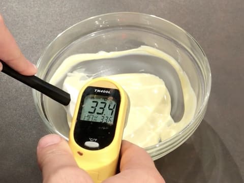 À L'aide d'un thermomètre à visée laser, prise de la température du chocolat blanc fondu dans le bol, qui titre 33,4°C, tout en étant mélangé avec la spatule maryse