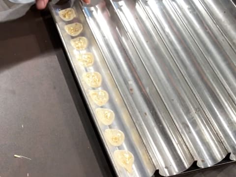 La bande de feuille guitare sur laquelle les pastilles de chocolat blanc pailletées sont apposées, est placée dans le creux d'une plaque à tuiles