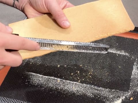 Le rectangle de biscuit en sablé breton est râpé à l'aide d'un zesteur-râpe