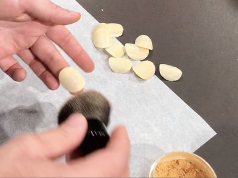 Les pastilles de chocolat blanc sont saupoudrées de colorant en poudre or, avec un pinceau à maquillage, au-dessus d'une feuille de papier sulfurisé