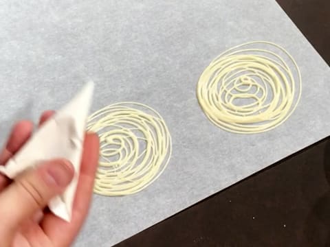 Deux spirales de chocolat blanc fondu sont formées sur une feuille de papier sulfurisé, à l'aide du cornet décor