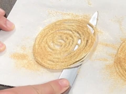 Une spirale de chocolat blanc dorée est décollée de la feuille de papier sulfurisé, avec la lame d'un couteau