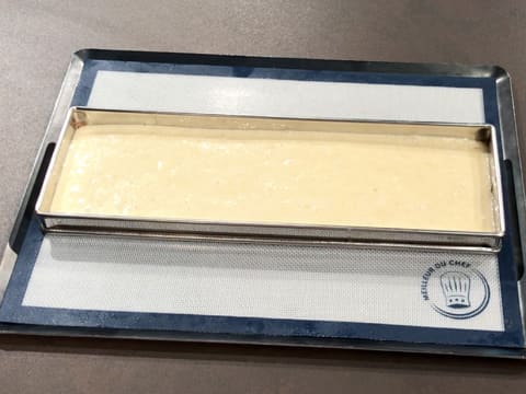 La préparation est égalisée dans le cadre inox rectangulaire qui est posé sur un tapis de cuisson en silicone, sur une plaque à pâtisserie