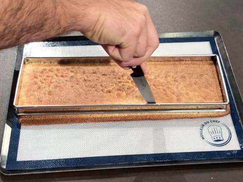 La lame d'un couteau est passée entre le biscuit aux pignons de pin et le cadre inox