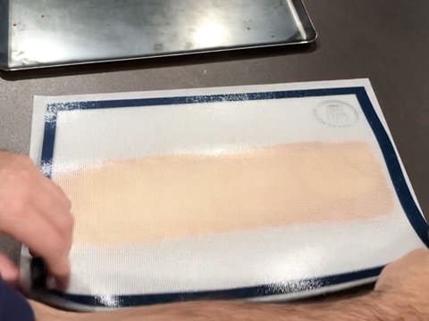 Le tapis de cuisson en silicone avec le biscuit aux pignons de pin, est retourné sur une feuille de papier sulfurisé, sur le plan de travail