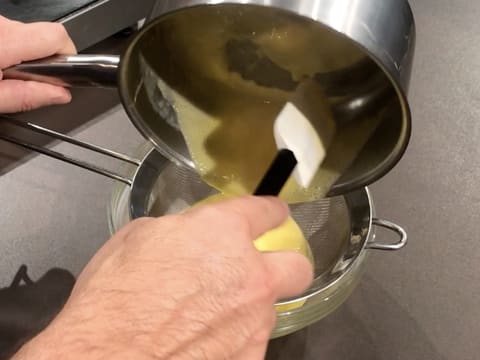 La préparation à base de Champagne, jus de citron, jaunes d'oeufs et sucre, est tamisée dans une passoire fine, au-dessus d'un bol