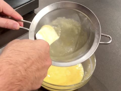 Le reste de la préparation à base de Champagne, jus de citron, jaunes d'oeufs et sucre, est écrasé avec la spatule maryse au fond de la passoire fine, au-dessus du bol