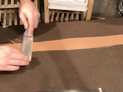 Le chocolat au lait fondu est étalé sur la bande de ruban pvc, à l'aide d'une spatule métallique coudée