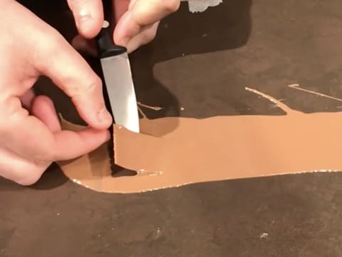 La bande de ruban pvc sur laquelle est étalé le chocolat au lait fondu, est soulevée par une extrémité, avec la pointe d'un couteau