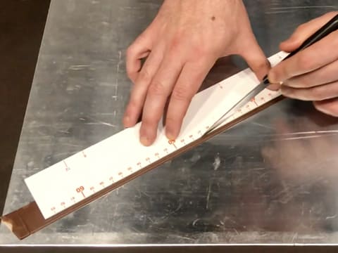 Une bande de chocolat au lait est mesurée avec une règle graduée et retaillée à l'aide d'un couteau