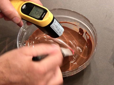 Prise de la température, à l'aide d'un thermomètre à visée laser, du chocolat au lait fondu qui est mélangé