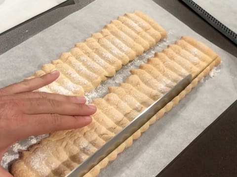 Un côté d'une bande de biscuit à la cuillère est paré à l'aide d'un couteau-scie à génoise