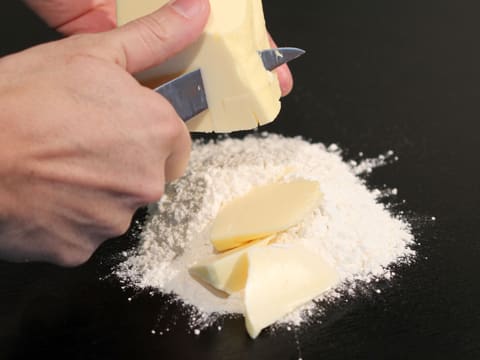 Du beurre est coupé en morceaux et ces morceaux sont placés sur de la farine qui a été versée sur le plan de travail
