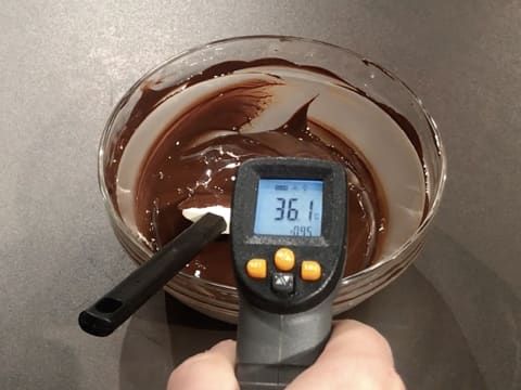 Prise de la température du chocolat noir fondu dans le saladier en verre, à l'aide d'un thermomètre à visée laser qui affiche 36,1°C