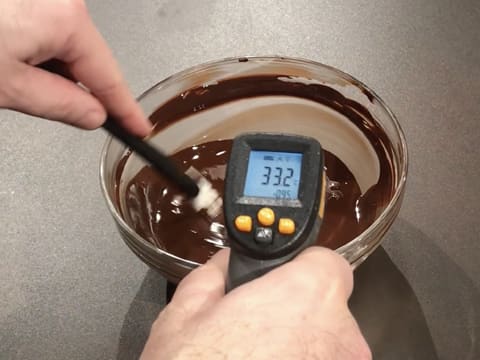 Prise de la température du chocolat noir fondu dans le saladier en verre, à l'aide d'un thermomètre à visée laser qui affiche 33,2°C