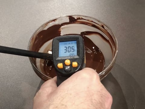 Prise de la température du chocolat noir fondu dans le saladier en verre, à l'aide d'un thermomètre à visée laser qui affiche 30,5°C