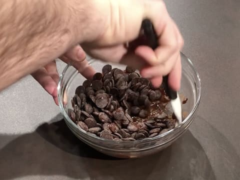 Les pistoles de chocolat noir sont en train de fondre dans le saladier en verre, tout en étant mélangées avec la spatule maryse