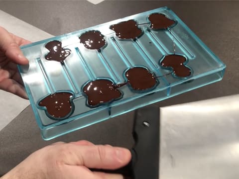 Le moule sucettes dont les cavités sont remplies de chocolat noir tempéré, est tapoté avec la spatule à chocolat