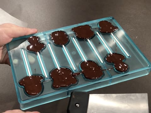 Le moule sucettes dont les cavités sont remplies de chocolat noir tempéré, est tapoté avec la spatule à chocolat