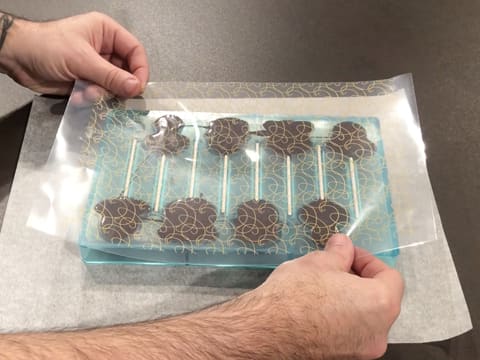 Une feuille transfert est déposée sur la surface du moule sucettes contre le chocolat noir tempéré