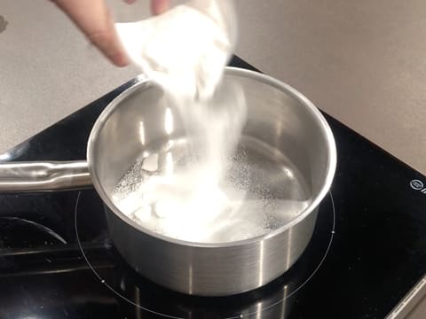 Du sucre en poudre est versé dans une casserole qui est posée sur la plaque de cuisson