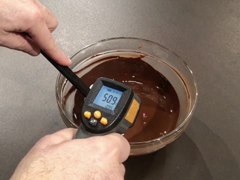 Prise de la température du chocolat noir fondu dans le saladier en verre, à l'aide d'un thermomètre à visée laser qui affiche 50,9°C