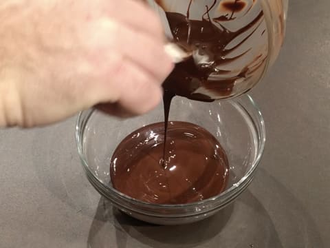 Le chocolat noir fondu est transvasé dans un autre saladier en verre qui est posé sur le plan de travail