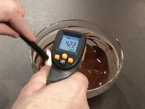 Prise de la température du chocolat noir fondu dans le saladier en verre, à l'aide d'un thermomètre à visée laser qui affiche 42,2°C