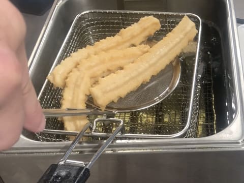 Les churros sont retirés de la friteuse à l'aide d'une écumoire