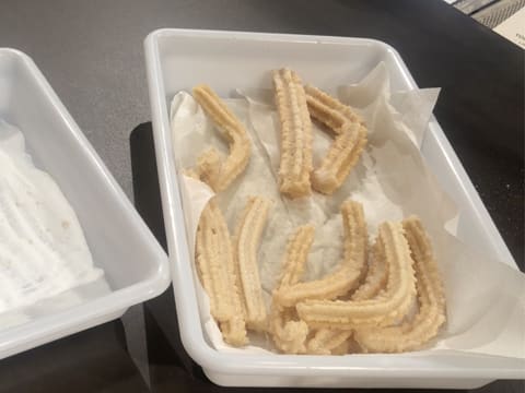 Obtention des churros enrobés de sucre en poudre et placés sur du papier absorbant dans un bac alimentaire