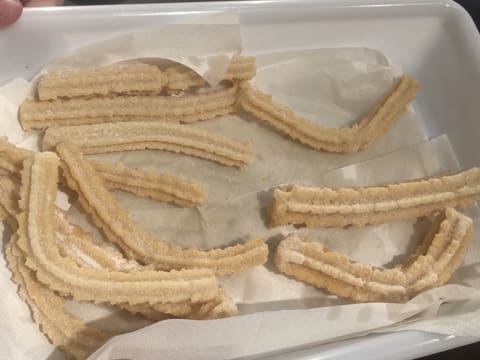 Obtention des churros enrobés de sucre en poudre et placés sur du papier absorbant dans un bac alimentaire