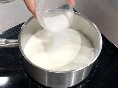 Du sucre en poudre est versé dans le lait qui se trouve dans la casserole sur la plaque de cuisson