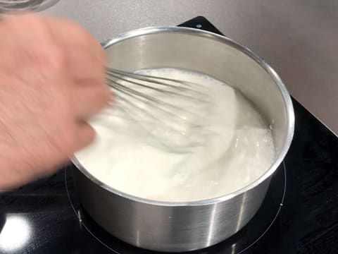 Le lait et le sucre sont mélangés au fouet dans la casserole qui est en train de chauffer sur la plaque de cuisson