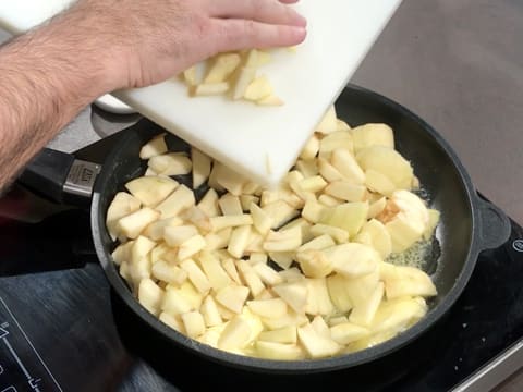 Les morceaux de pommes sont versés dans la poêle qui est placée sur une plaque de cuisson
